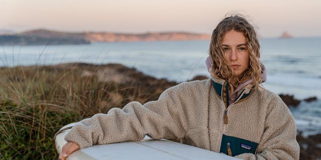 Mädchen mit Surfboard umgeben von Stranddünen