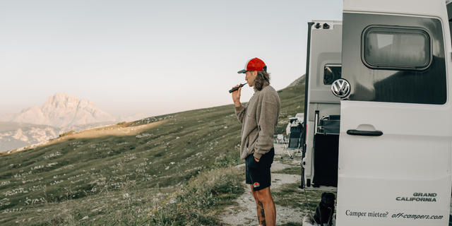 Ein Mann putzt sich vor dem Camper in den Bergen die Zähne.