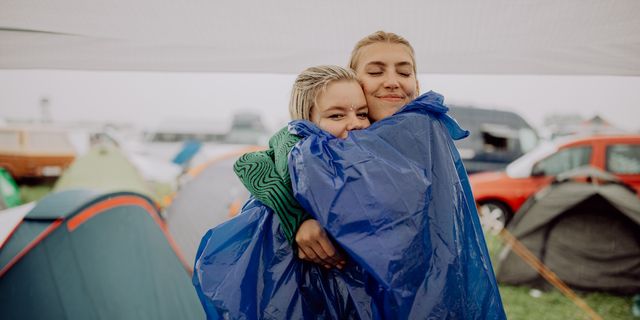 Two women are hugging at a festival site, with cars and tents visible around them. Here you’ll find our festival packing list.