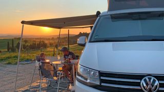Father sits with his son in front of a camper in Tuscany and enjoys the sunset.
