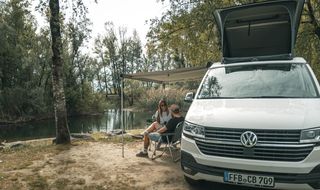 Paar sitzt vor VW T6 an einem See