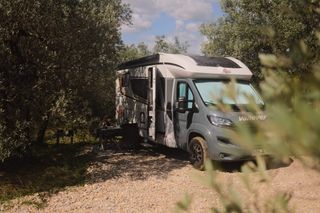 A camper is parked by the trees